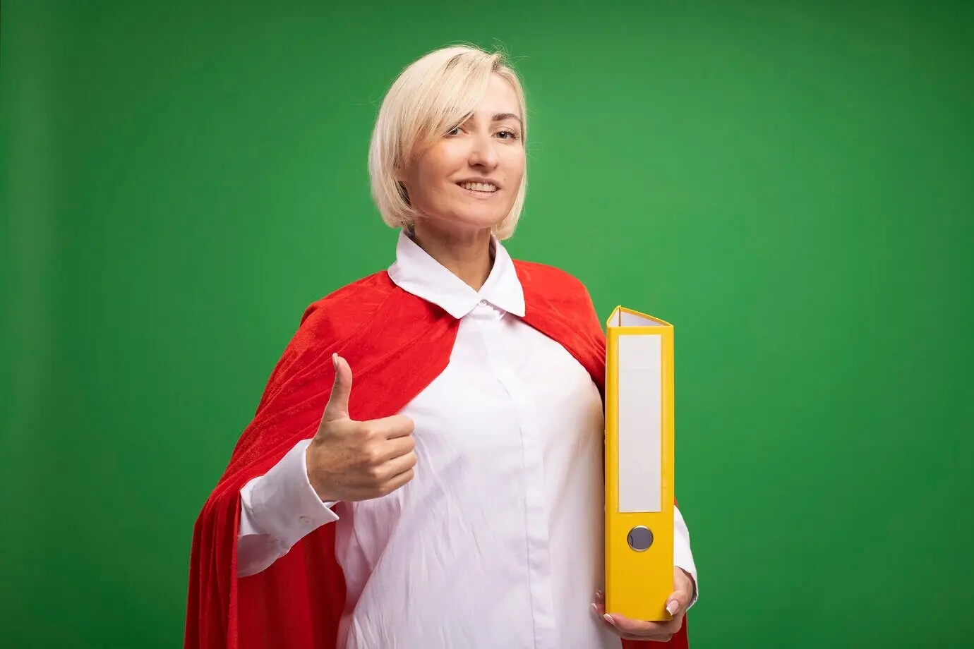 緑の壁の前のコピースペースのある背景で、赤いマントを身に着け、フォルダーを手に持ち親指を立てている、笑顔の中年の金髪の女性スーパーヒーロー。
